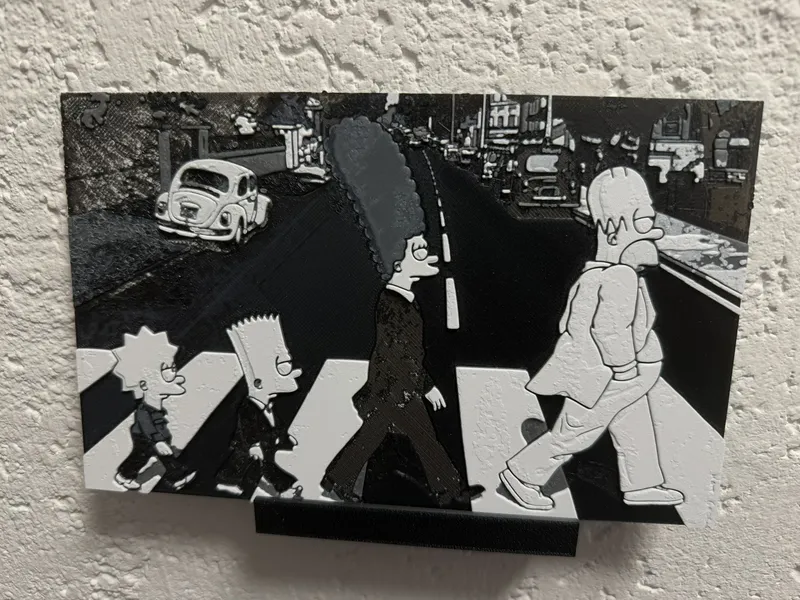 HueForge-Druck an der Wand – die vier Simpsons überqueren in Schwarz-Weiß einen Zebrastreifen im Abbey-Road-Motiv, dahinter ein VW Käfer und eine Straßenzeile