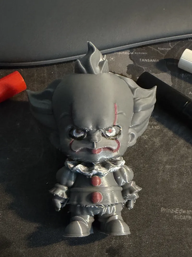 Chibi-Figur eines Clowns aus grauem PLA, direkt mit Acryl-Stiften bemalt – rote Linien im Gesicht, rote Knöpfe am Kostüm; daneben liegen die verwendeten Stifte